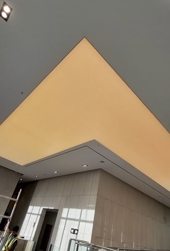 Architectural stretch ceiling featuring a printed translucent membrane and concealed LED lighting for a modern lobby interior. Architectural stretch ceiling featuring a printed translucent membrane and concealed LED lighting for a modern lobby interior.