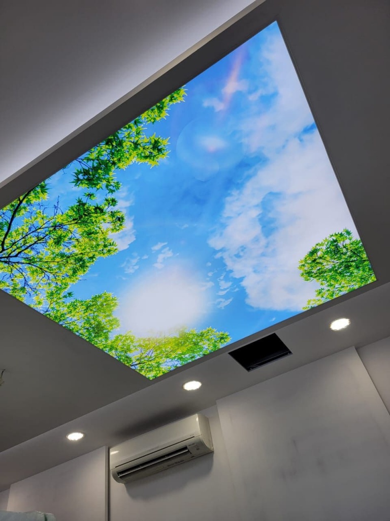 Printed illuminated stretch ceiling featuring a blue sky and green tree canopy, creating the effect of an open skylight in a modern Dubai interior. Printed illuminated stretch ceiling featuring a blue sky and green tree canopy, creating the effect of an open skylight in a modern Dubai interior.