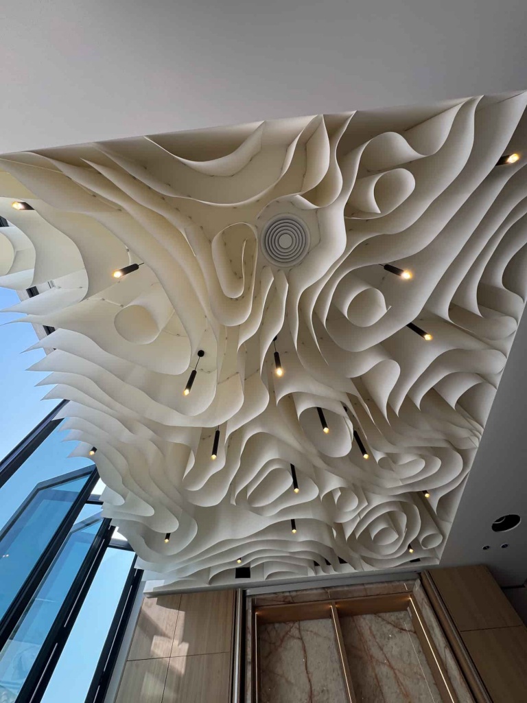 Detailed perspective of a flowing architectural fabric ceiling with suspended cylindrical elements and integrated spotlights. The custom installation combines innovative fabric engineering with contemporary design, creating a luxurious feature ceiling for high-end residential projects in Dubai. Detailed perspective of a flowing architectural fabric ceiling with suspended cylindrical elements and integrated spotlights. The custom installation combines innovative fabric engineering with contemporary design, creating a luxurious feature ceiling for high-end residential projects in Dubai.