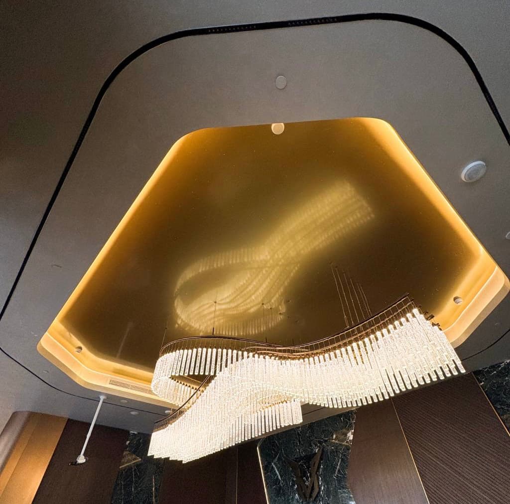 Luxury gold reflective stretch ceiling with warm perimeter lighting and statement crystal chandelier creating an elegant decorative ceiling feature. Luxury gold reflective stretch ceiling with warm perimeter lighting and statement crystal chandelier creating an elegant decorative ceiling feature.