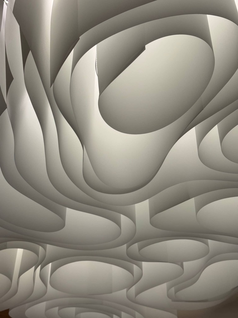 Night view of the illuminated architectural fabric ceiling showing concealed LED lighting that enhances the sculptural geometry of the installation. Night view of the illuminated architectural fabric ceiling showing concealed LED lighting that enhances the sculptural geometry of the installation.