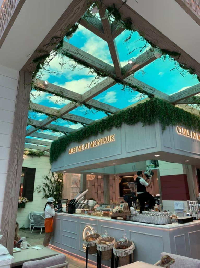 Restaurant interior featuring a printed Sky Ceiling with decorative timber pergola beams, artificial greenery and seamless LED backlighting. Restaurant interior featuring a printed Sky Ceiling with decorative timber pergola beams, artificial greenery and seamless LED backlighting.