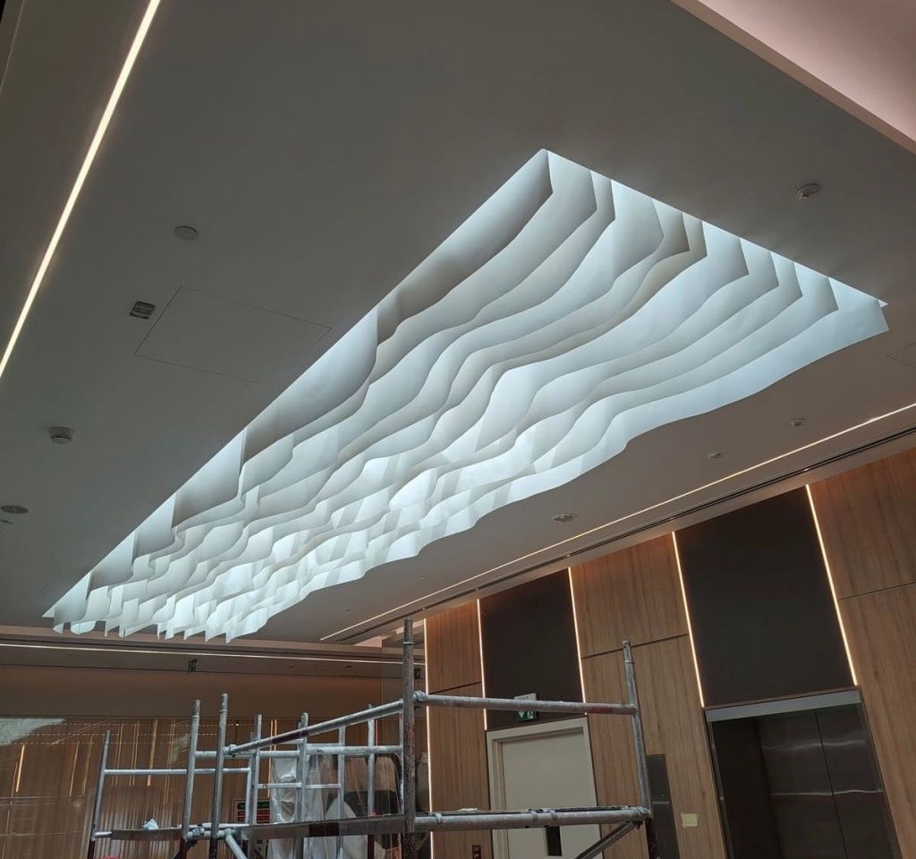 Close-up view of an organic sculptural ceiling featuring layered fabric forms and warm backlighting that emphasizes depth and curved geometry. Close-up view of an organic sculptural ceiling featuring layered fabric forms and warm backlighting that emphasizes depth and curved geometry.