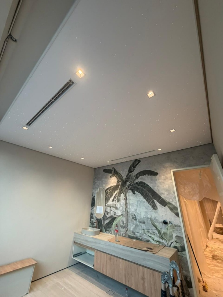 White stretch ceiling with subtle fiber optic stars integrated with recessed lighting and linear air-conditioning grille. White stretch ceiling with subtle fiber optic stars integrated with recessed lighting and linear air-conditioning grille.