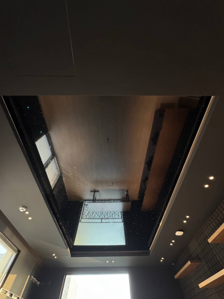 Reflective black mirror stretch ceiling with fiber optic star lighting creating a premium entertainment space. Reflective black mirror stretch ceiling with fiber optic star lighting creating a premium entertainment space.