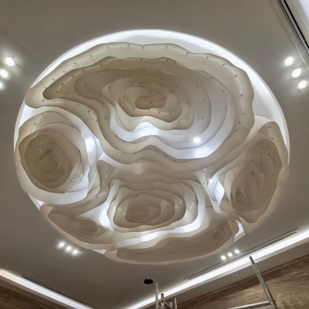 Large-scale sculptural fabric ceiling created from repeated curved fabric elements with warm indirect lighting, producing a dramatic architectural feature. Large-scale sculptural fabric ceiling created from repeated curved fabric elements with warm indirect lighting, producing a dramatic architectural feature.