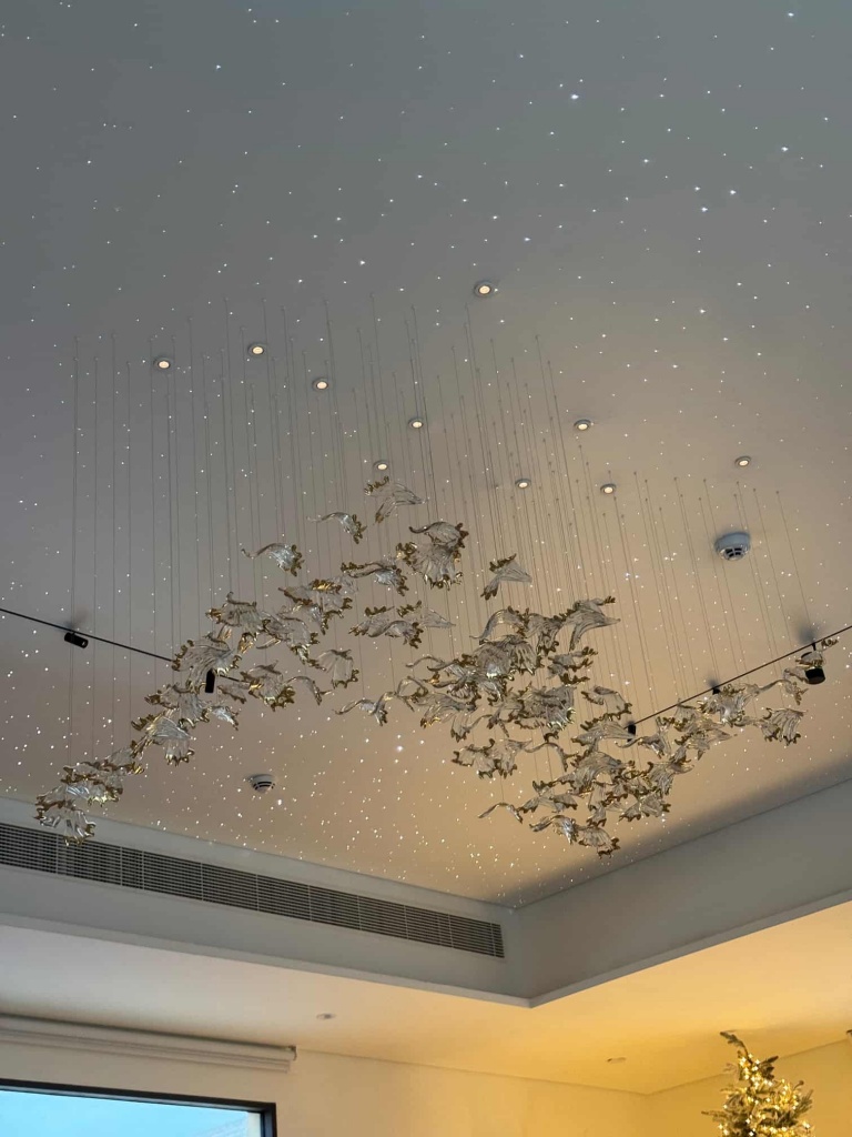 Luxury white stretch ceiling featuring hundreds of fiber optic stars and a custom designer chandelier installed in a premium villa in Abu Dhabi. The project combines elegant architectural lighting with a seamless modern ceiling design. Luxury white stretch ceiling featuring hundreds of fiber optic stars and a custom designer chandelier installed in a premium villa in Abu Dhabi. The project combines elegant architectural lighting with a seamless modern ceiling design.