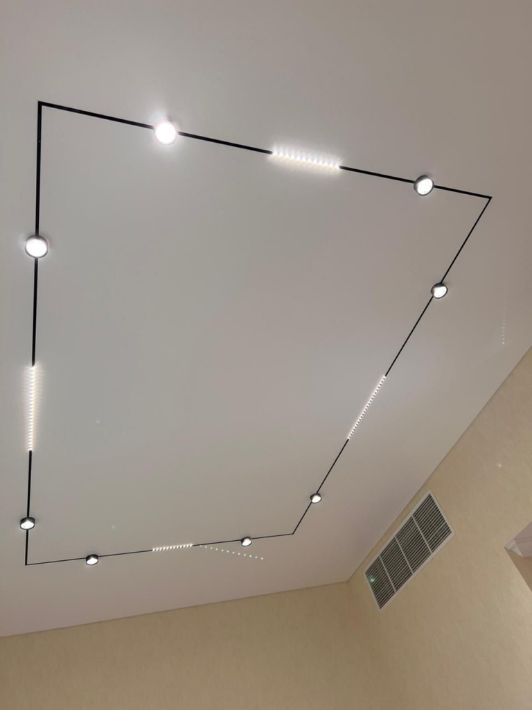 Contemporary white stretch ceiling featuring a geometric black magnetic track system, integrated linear lighting and decorative chandelier in a modern villa interior. Contemporary white stretch ceiling featuring a geometric black magnetic track system, integrated linear lighting and decorative chandelier in a modern villa interior.