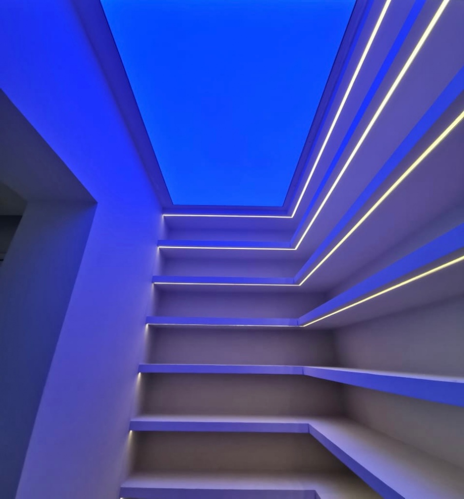 Custom RGBW stretch ceiling with blue ambient illumination and integrated linear LED lighting for a modern residential interior. Custom RGBW stretch ceiling with blue ambient illumination and integrated linear LED lighting for a modern residential interior.
