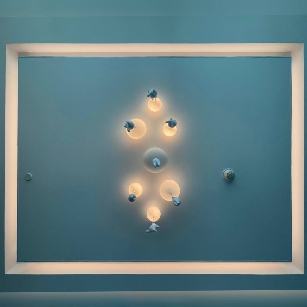 Seamless white stretch ceiling featuring integrated perimeter lighting and a decorative chandelier for a luxury nursery interior. Seamless white stretch ceiling featuring integrated perimeter lighting and a decorative chandelier for a luxury nursery interior.