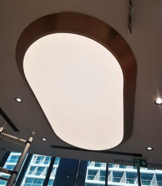 Custom organic-shaped luminous ceiling panel installed above a hospital reception area, providing seamless LED illumination and a premium architectural focal point. Custom organic-shaped luminous ceiling panel installed above a hospital reception area, providing seamless LED illumination and a premium architectural focal point.