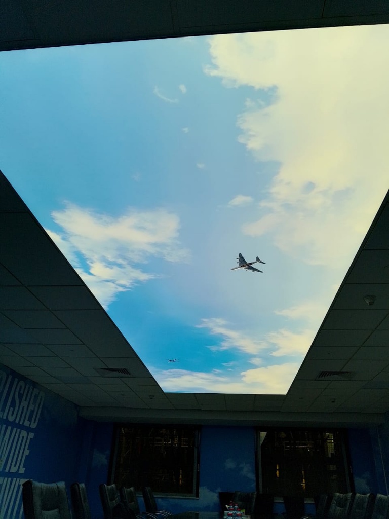 Illuminated stretch ceiling with a custom sky print installed in a commercial office, creating a bright and spacious atmosphere. Illuminated stretch ceiling with a custom sky print installed in a commercial office, creating a bright and spacious atmosphere.