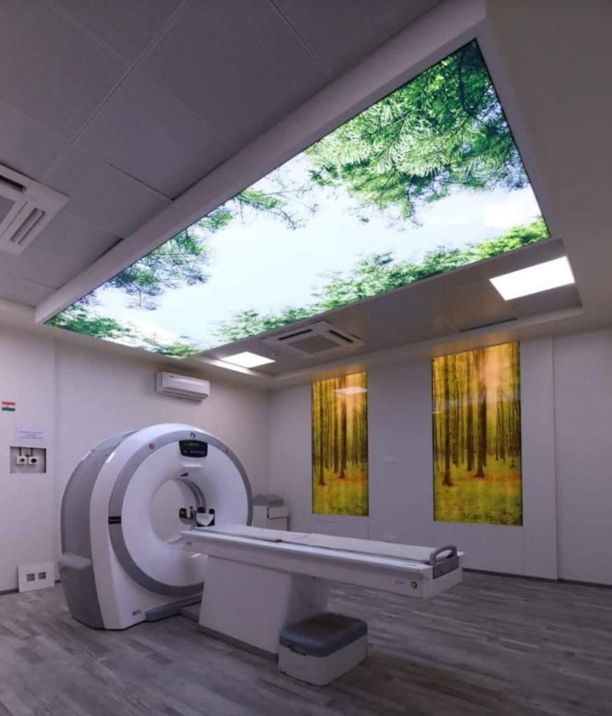 Printed stretch ceiling installed above an MRI scanner with a calming forest sky design to improve patient comfort in a medical facility. Printed stretch ceiling installed above an MRI scanner with a calming forest sky design to improve patient comfort in a medical facility.