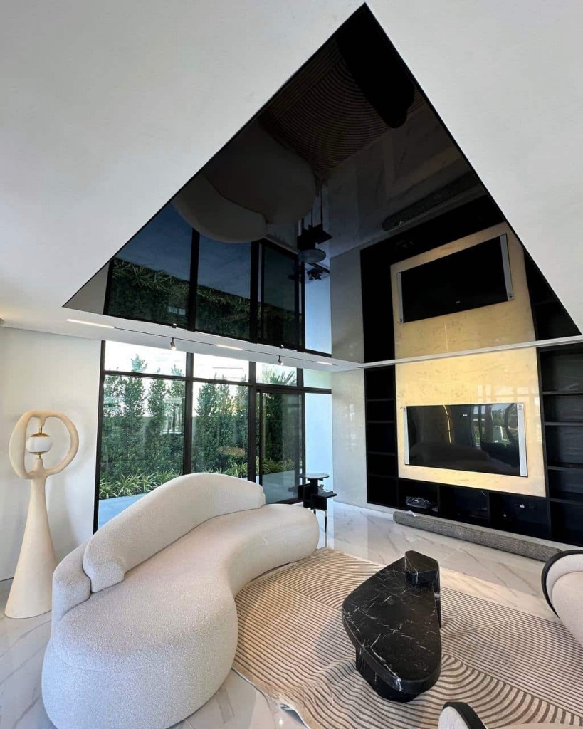 Large black glossy stretch ceiling creating a dramatic mirror effect and visual depth in a contemporary luxury villa living room. Large black glossy stretch ceiling creating a dramatic mirror effect and visual depth in a contemporary luxury villa living room.